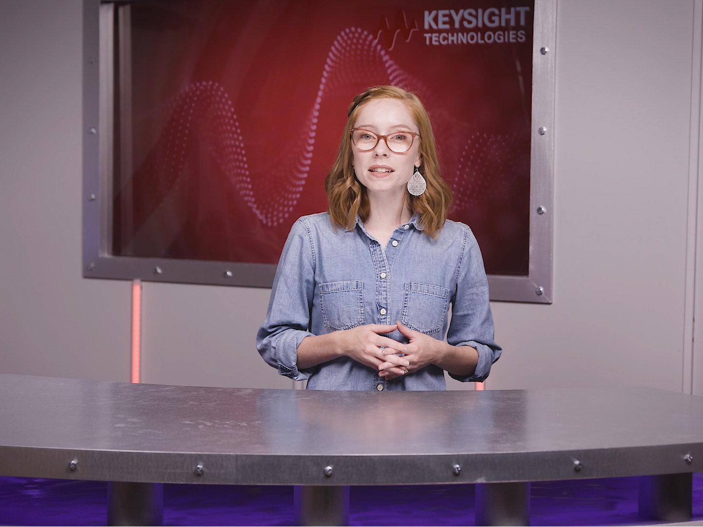 Young woman with brown hair, standing in front of a large screen displaying “Keysight Technologies” in the top right. decoding=