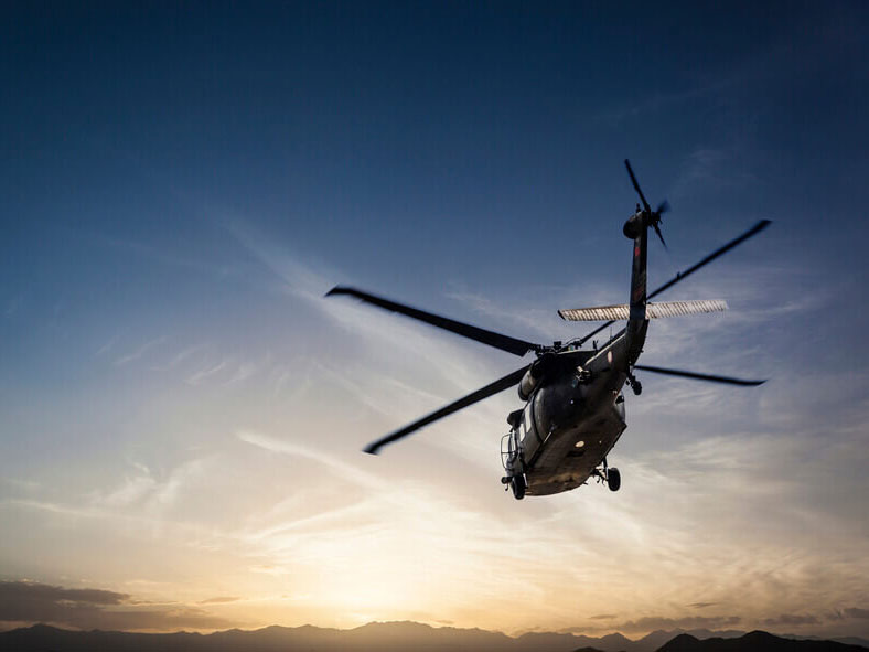 Military helicopter flying with the sun close to the horizon in the background.