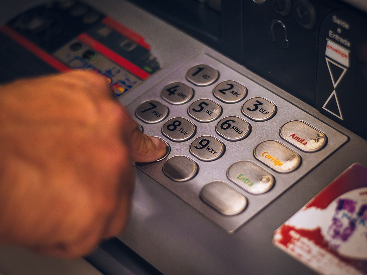 Close-up of a right hand pressing a button on an ATM keypad.