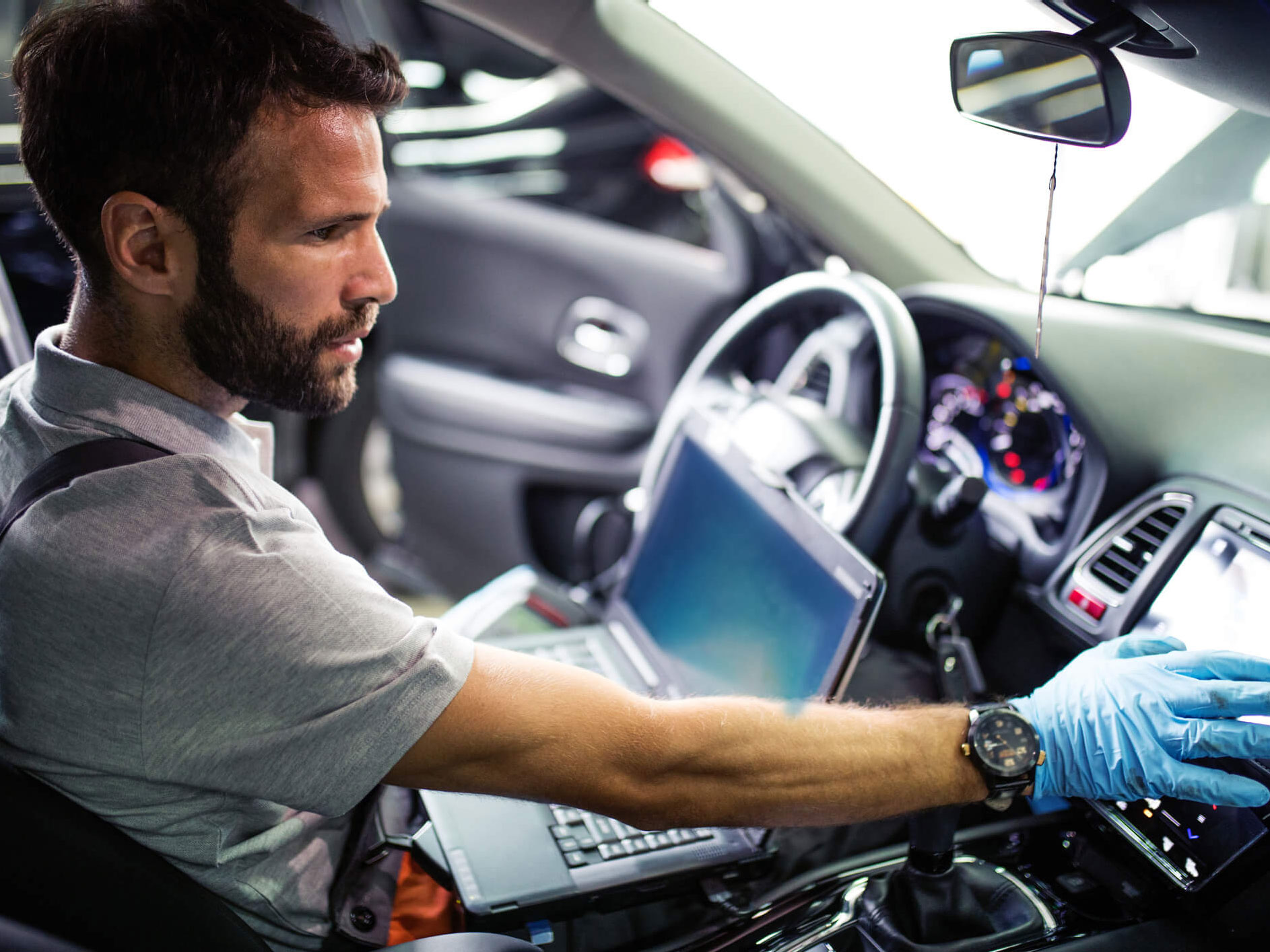 Bearded white male sitting in a car with an open laptop, testing the device mounted next to the steering wheel.