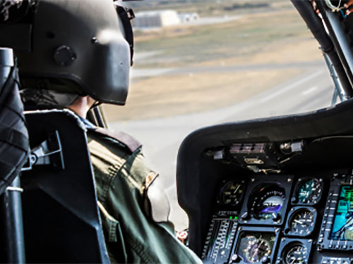 Military helicopter pilot wearing helmet and sitting in an airplane cockpit.