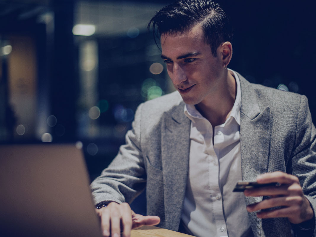 Young man in blazer and white shirt, holding a credit card with his other hand on a laptop keyboard.