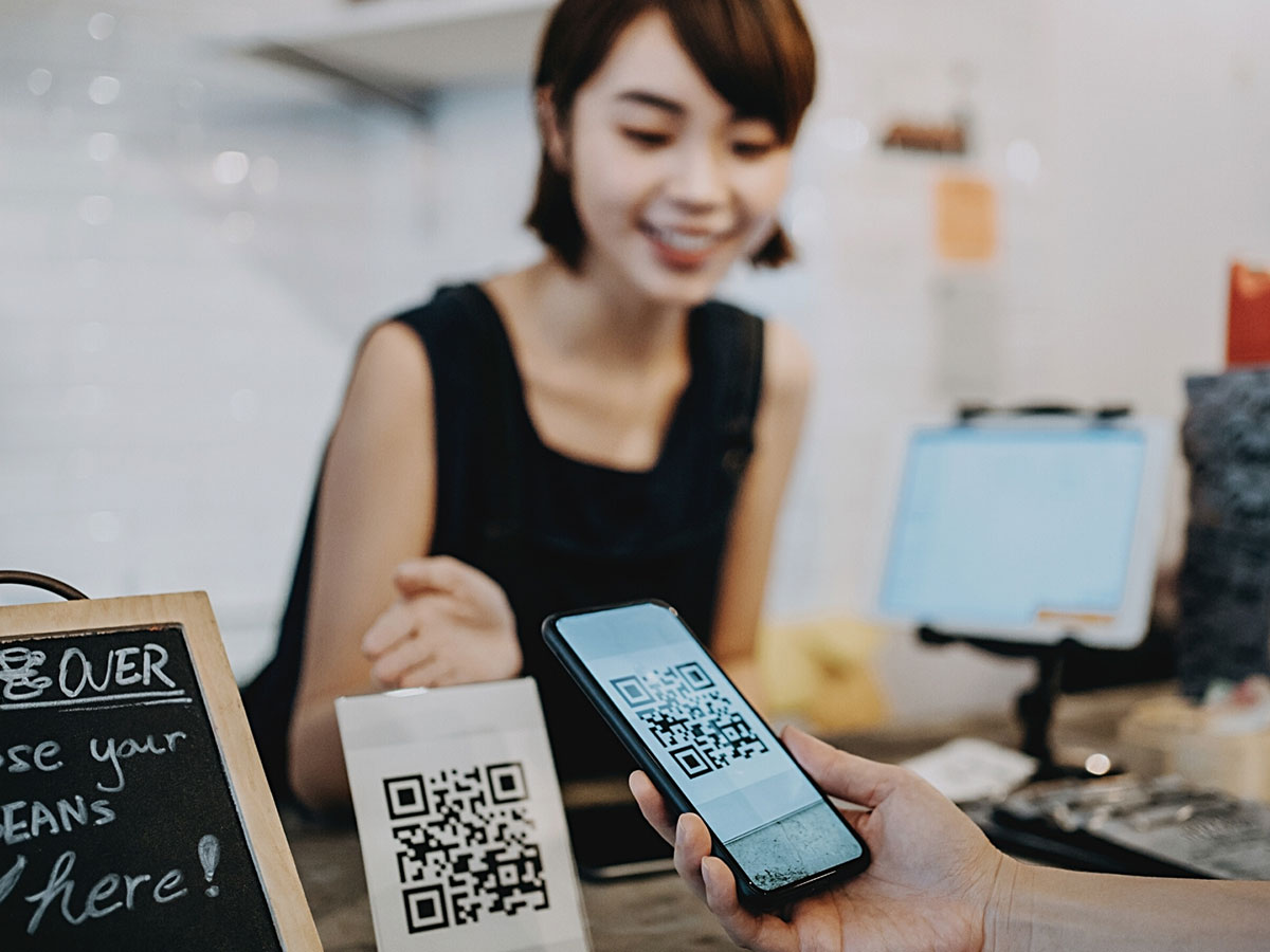 Young Asian woman looking at a mobile phone being held by another person using phone camera to scan a QR code.